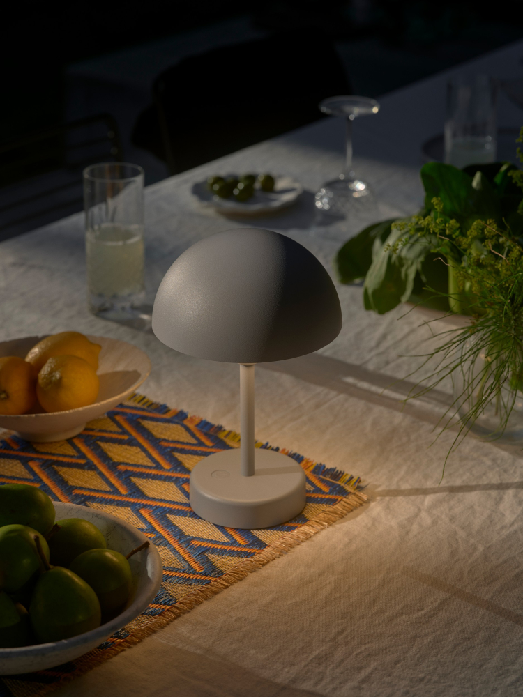 Oliven Grün Akkuleuchte Nordlux Ellen To-Go auf dem Tisch neben der Ladestation